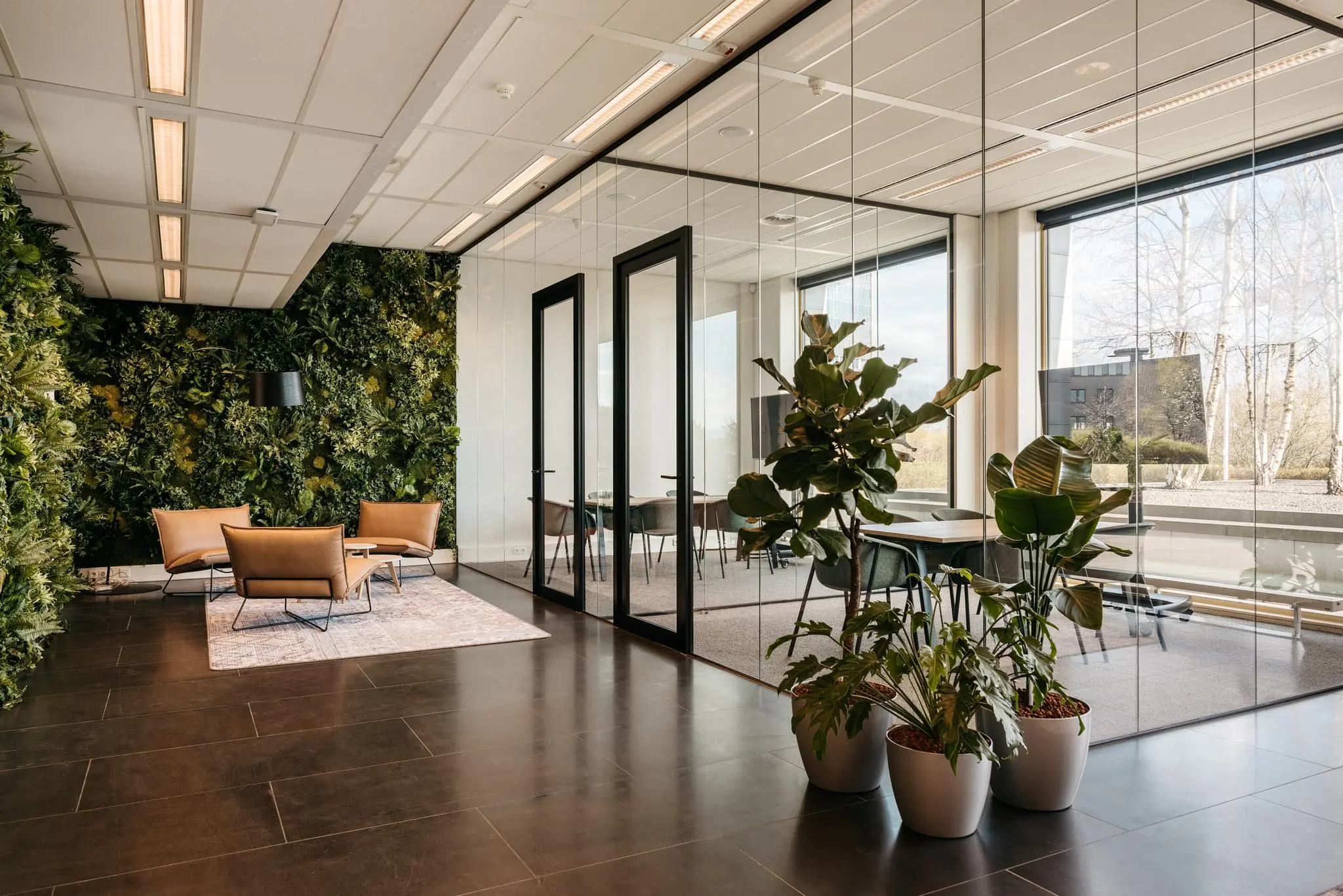 Moderne kantoorruimte aan de Fascinatio Boulevard met glazen vergaderruimtes, groene plantenwand en een zithoek met leren stoelen.